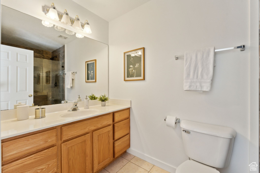 Full bath with vanity, tiled shower, toilet, tile patterned flooring, and baseboards