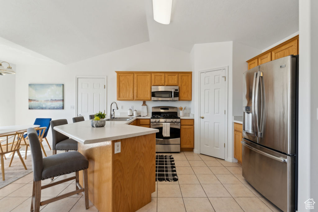 Kitchen featuring appliances with stainless steel finishes, a peninsula, light tile patterned flooring, a kitchen breakfast bar, and high vaulted ceiling
