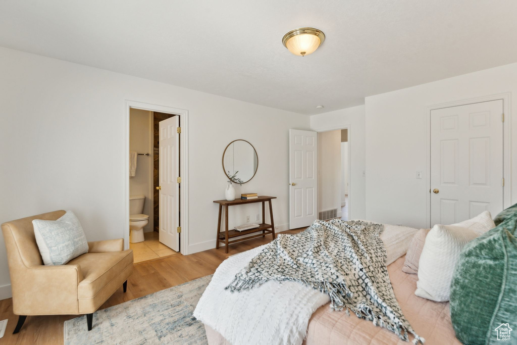 Bedroom with light wood finished floors, ensuite bathroom, and baseboards