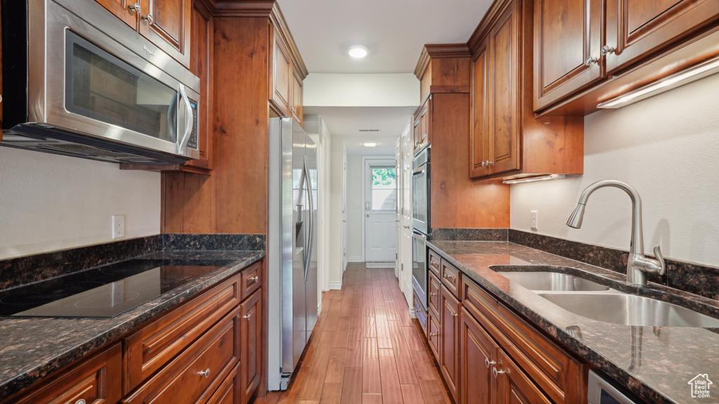 Kitchen with stainless steel appliances, a sink, brown cabinets, dark stone counters, and light wood-style flooring