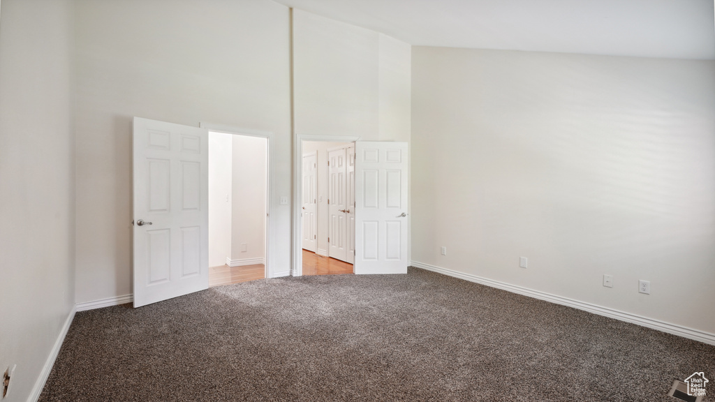 Unfurnished bedroom featuring light carpet, a high ceiling, and baseboards