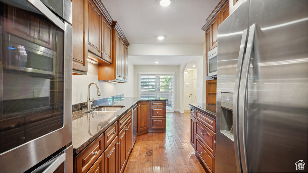Kitchen featuring appliances with stainless steel finishes, a sink, light wood-style floors, dark stone countertops, and brown cabinets