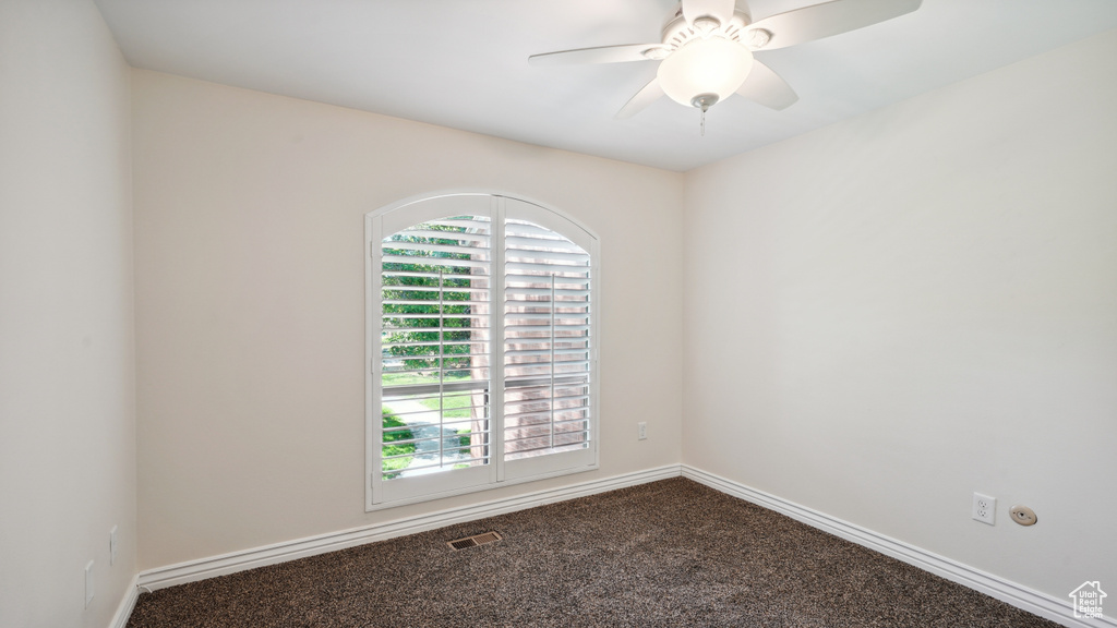 Unfurnished room featuring dark colored carpet, baseboards, and a ceiling fan