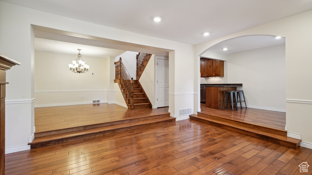 Unfurnished living room with wood-type flooring, stairway, recessed lighting, a chandelier, and arched walkways