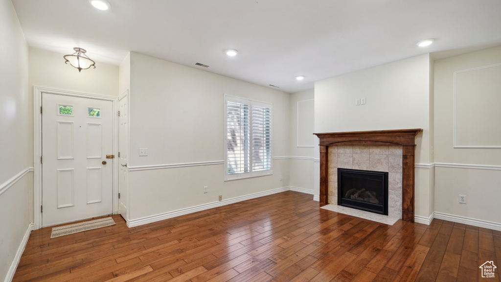 Unfurnished living room with hardwood / wood-style floors, a tiled fireplace, baseboards, and recessed lighting