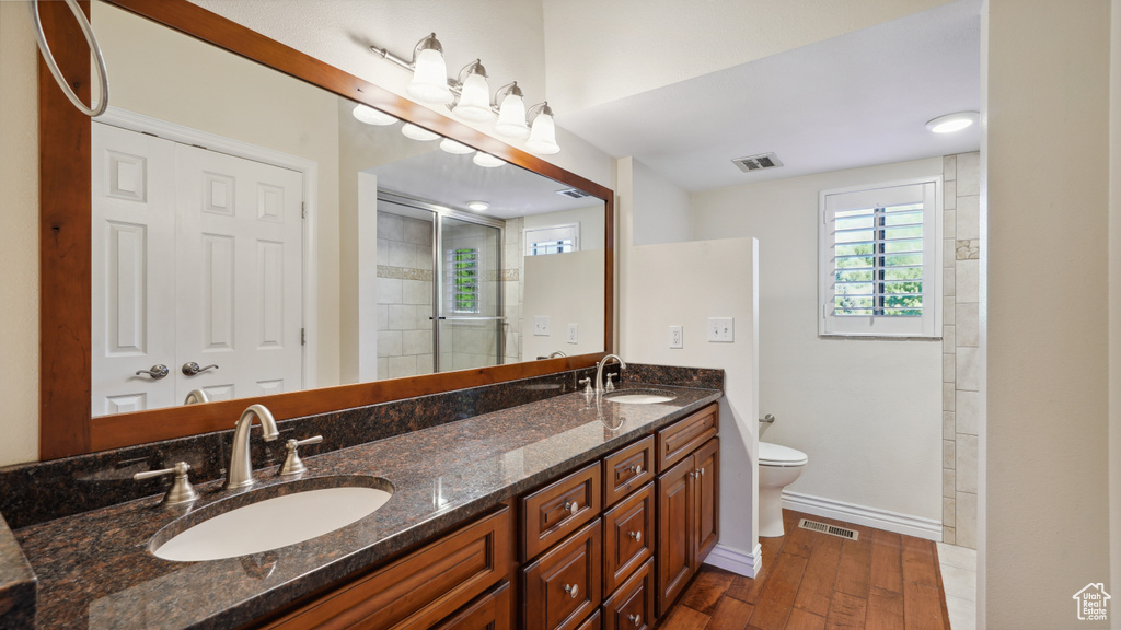 Full bathroom featuring toilet, wood finished floors, double vanity, baseboards, and tiled shower