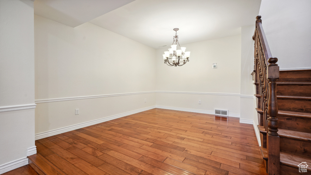 Empty room with hardwood / wood-style flooring, stairs, baseboards, and a chandelier