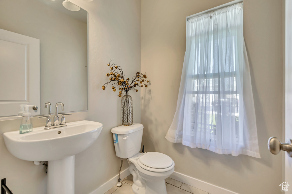 Half bathroom featuring toilet, tile patterned floors, baseboards, and a sink