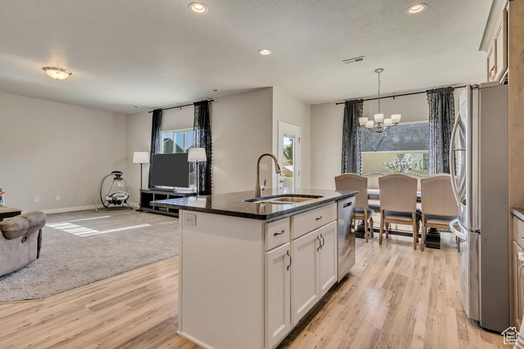 Kitchen featuring stainless steel appliances, a sink, a chandelier, open floor plan, and white cabinets