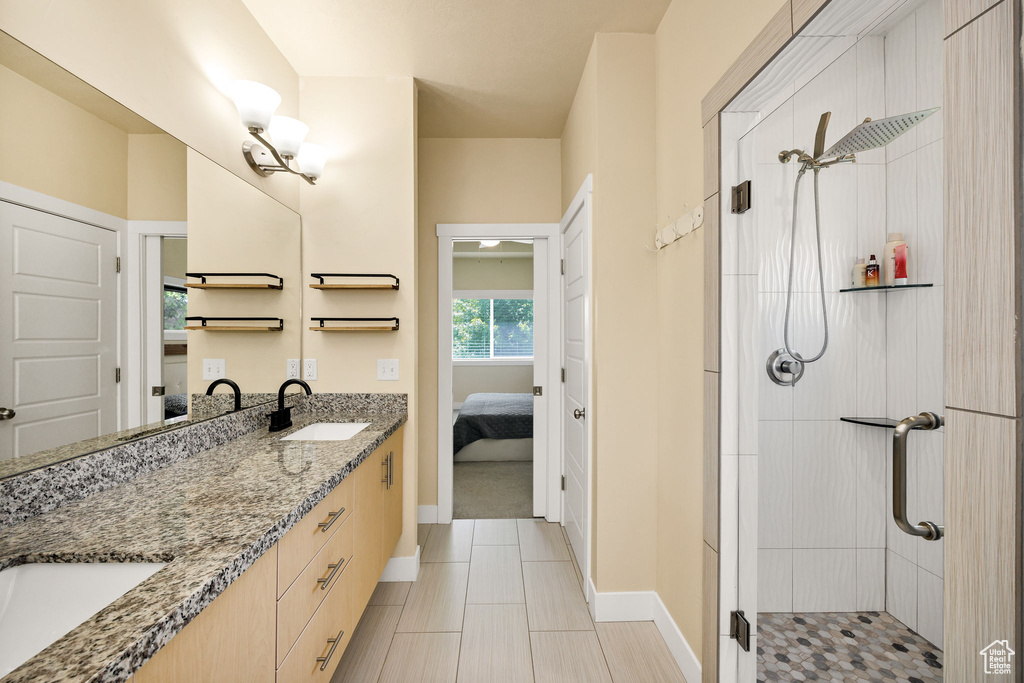 Full bath with connected bathroom, double vanity, a stall shower, and baseboards