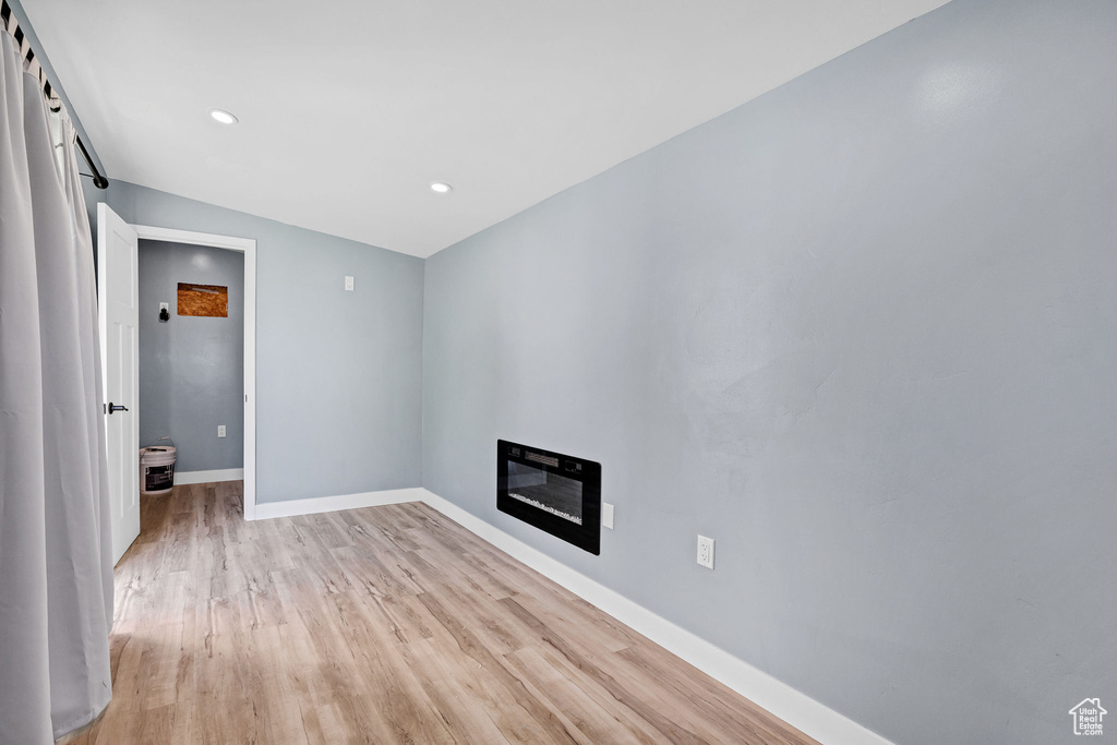 Unfurnished living room featuring light wood-style flooring, baseboards, recessed lighting, a glass covered fireplace, and heating unit