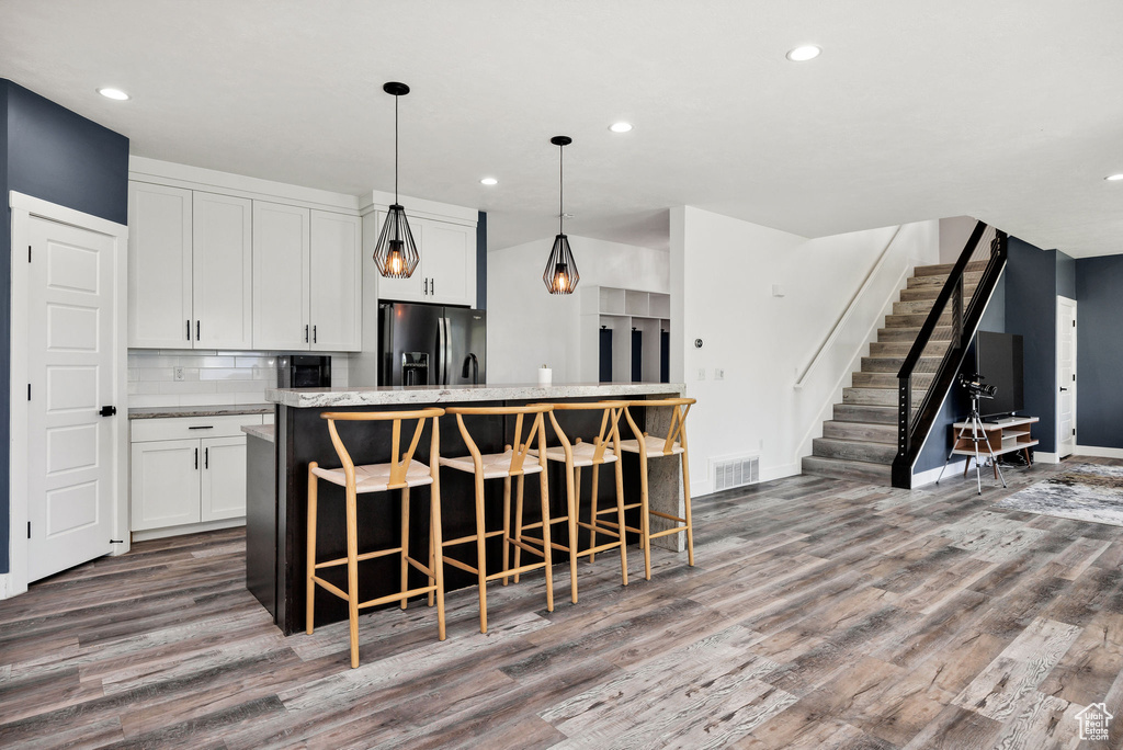Kitchen with refrigerator with ice dispenser, wood finished floors, a kitchen island, white cabinets, and recessed lighting