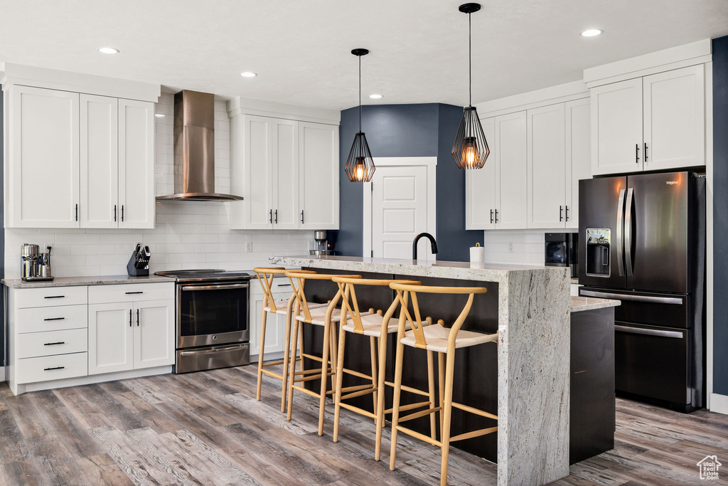 Kitchen with refrigerator with ice dispenser, wall chimney range hood, stainless steel electric range, backsplash, and wood finished floors