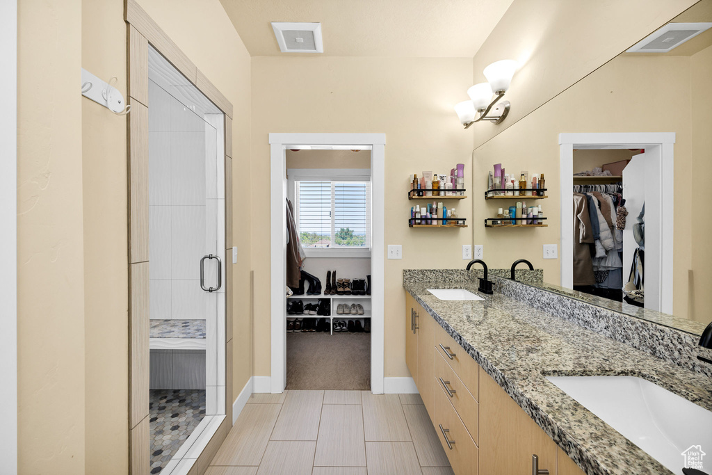 Bathroom featuring a stall shower, double vanity, a walk in closet, and baseboards
