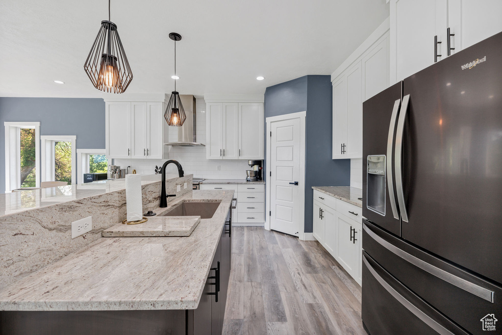 Kitchen with refrigerator with ice dispenser, wall chimney range hood, decorative backsplash, a sink, and recessed lighting