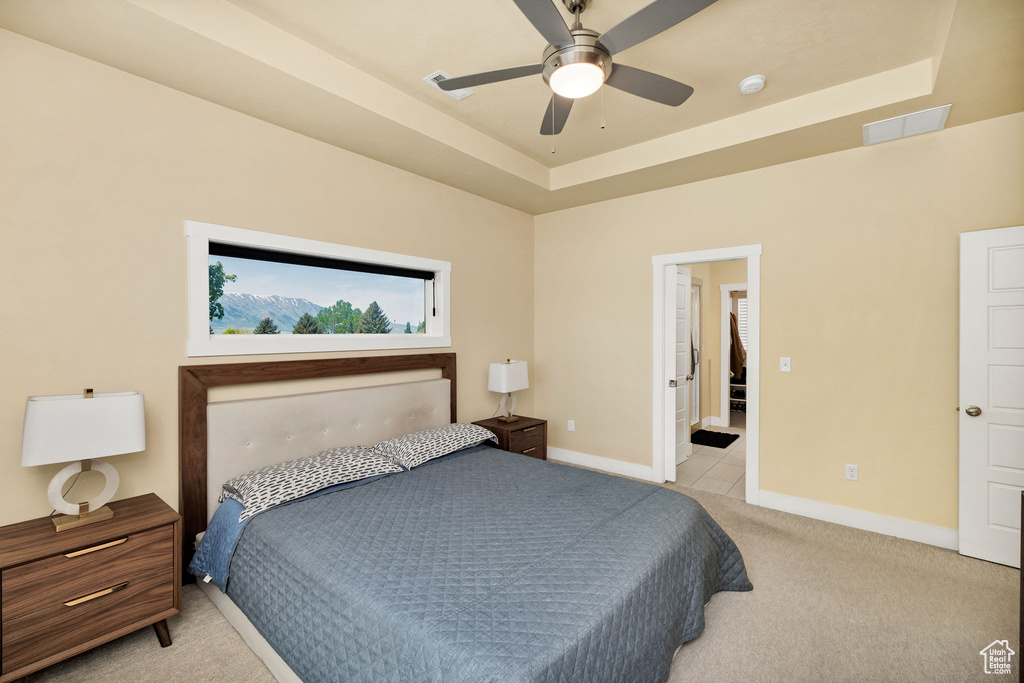 Bedroom featuring light colored carpet, baseboards, a raised ceiling, and a ceiling fan