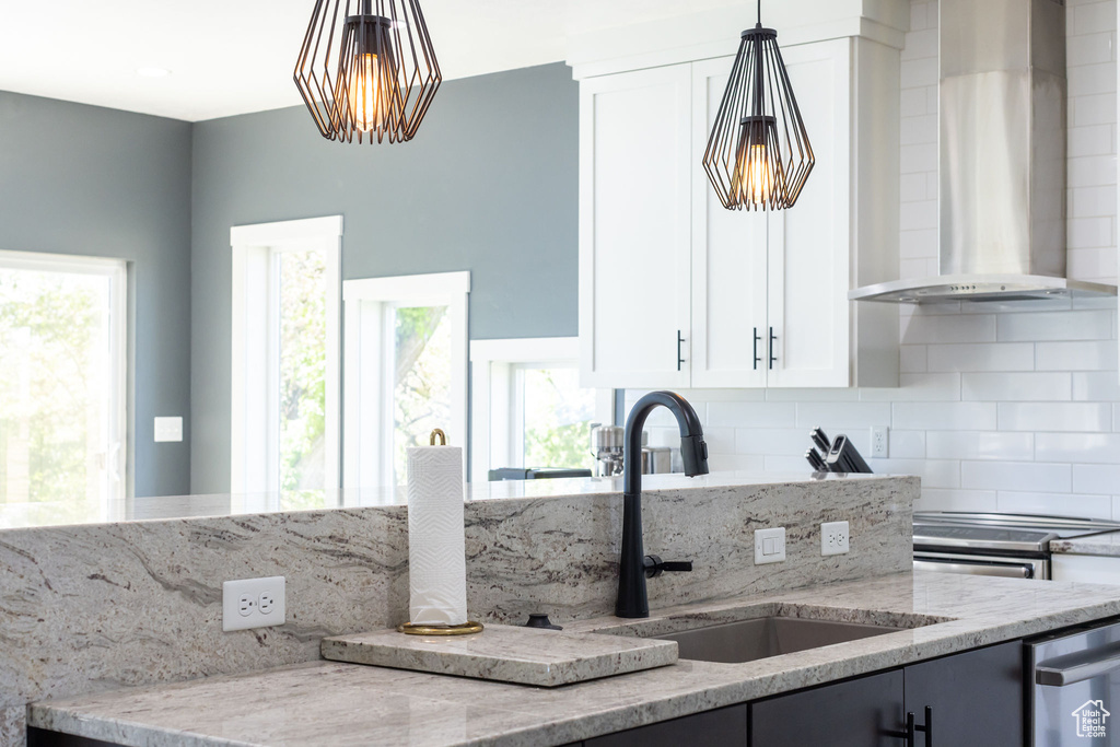 Kitchen featuring wall chimney exhaust hood, a sink, light stone counters, tasteful backsplash, and healthy amount of natural light