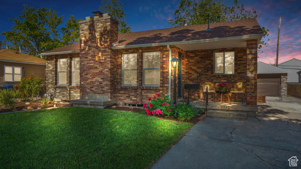 Bungalow with a front yard, a chimney, a porch, a shingled roof, and brick siding