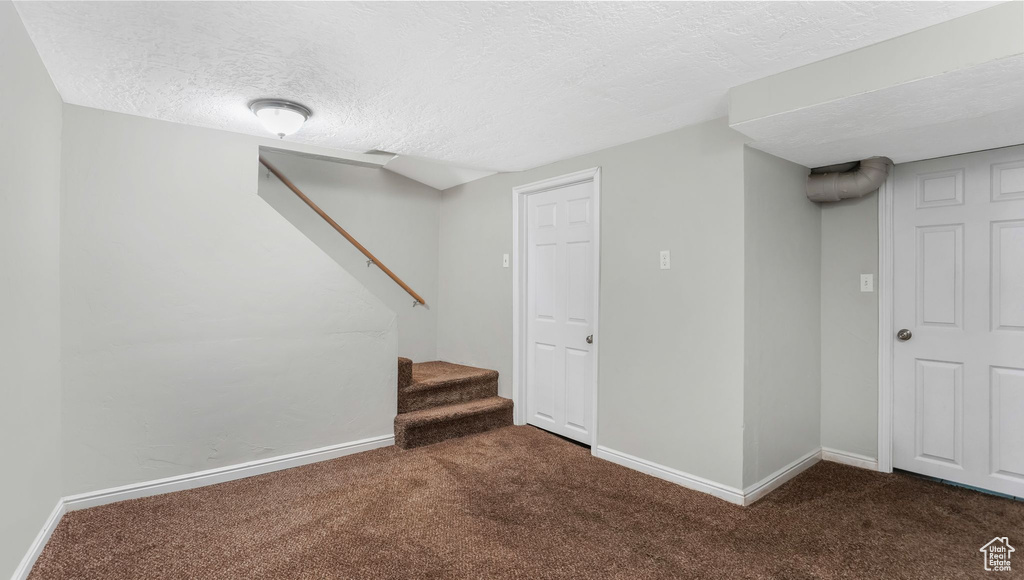 Finished below grade area with carpet, a textured ceiling, baseboards, and stairs