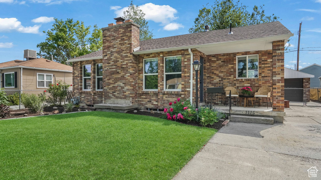 View of front of home featuring a chimney, a shingled roof, a porch, brick siding, and central AC