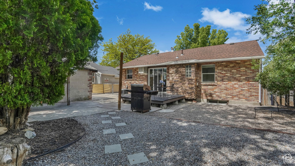 Back of house featuring a deck, a patio, brick siding, and roof with shingles
