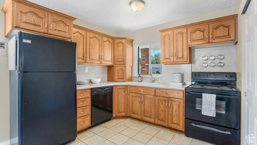 Kitchen featuring black appliances, a sink, light countertops, light tile patterned floors, and a textured ceiling