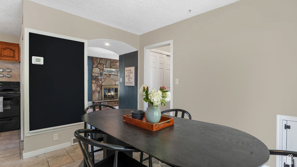 Dining area with a textured ceiling, light tile patterned floors, baseboards, a fireplace, and arched walkways