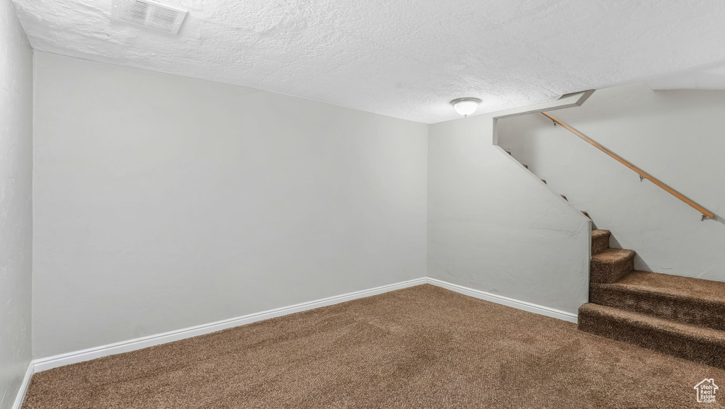 Finished below grade area with carpet flooring, a textured ceiling, stairs, and baseboards