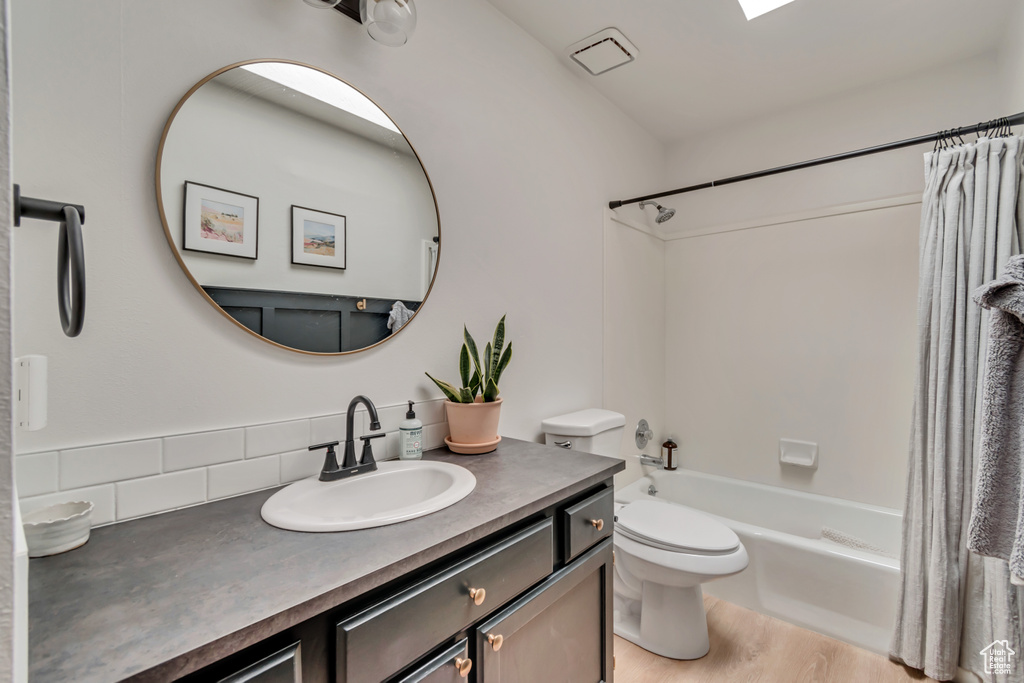 Bathroom featuring vanity, shower / bath combo, toilet, wood finished floors, and decorative backsplash