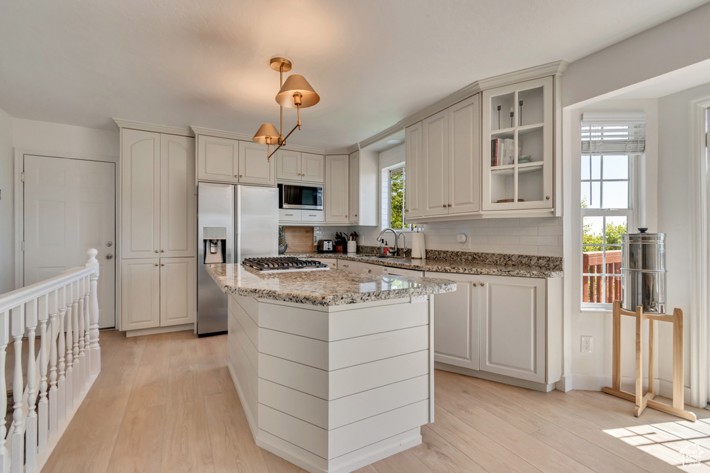 Kitchen featuring stainless steel appliances, a sink, light wood finished floors, and glass insert cabinets