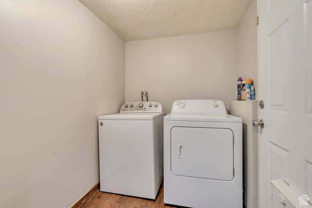 Laundry area with washing machine and dryer, light wood-style flooring, a textured ceiling, and baseboards