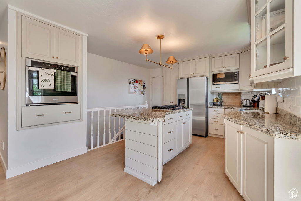 Kitchen featuring stainless steel appliances, light wood finished floors, a kitchen island, a sink, and decorative backsplash