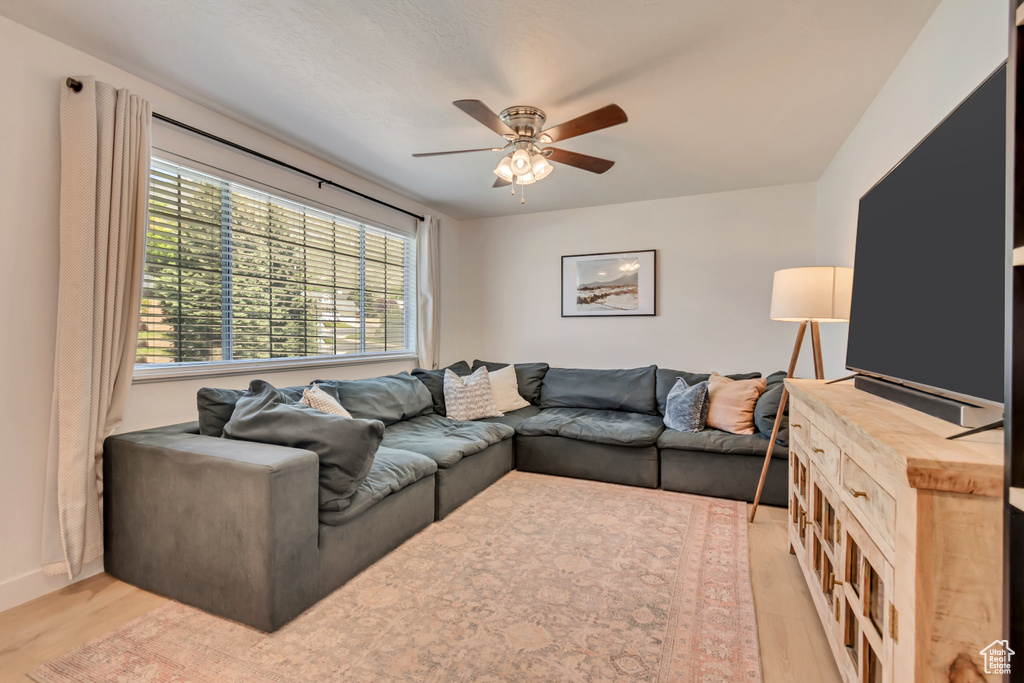 Living room with a ceiling fan, light wood finished floors, and baseboards