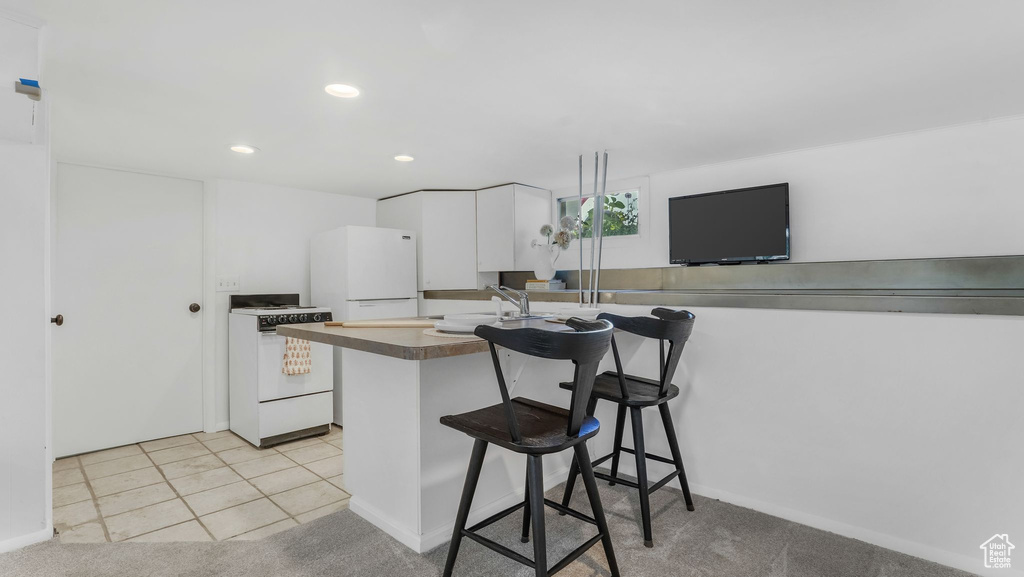 Kitchen with white appliances, white cabinetry, a kitchen breakfast bar, recessed lighting, and baseboards