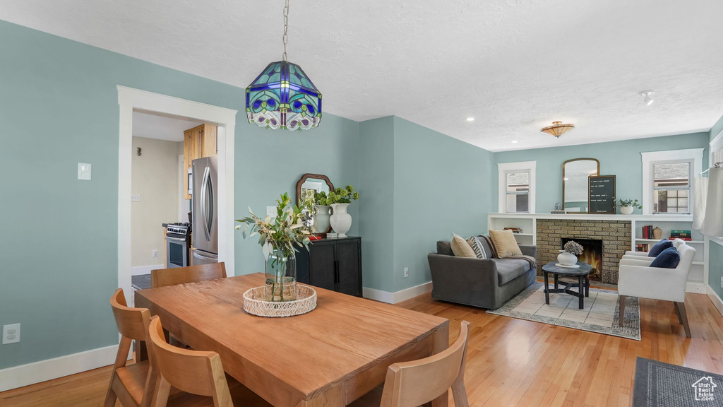 Dining space with baseboards, a textured ceiling, a brick fireplace, light wood-type flooring, and recessed lighting