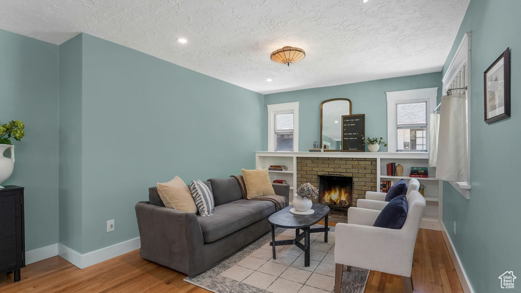 Living area with a textured ceiling, light wood-type flooring, baseboards, a fireplace, and plenty of natural light