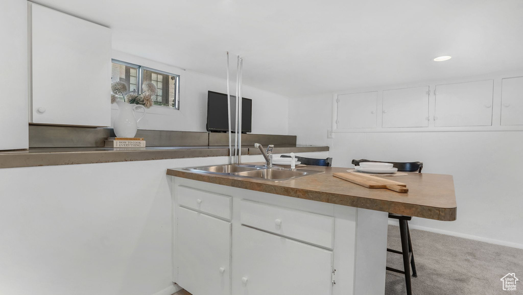 Kitchen featuring a sink, white cabinets, a kitchen bar, carpet, and recessed lighting