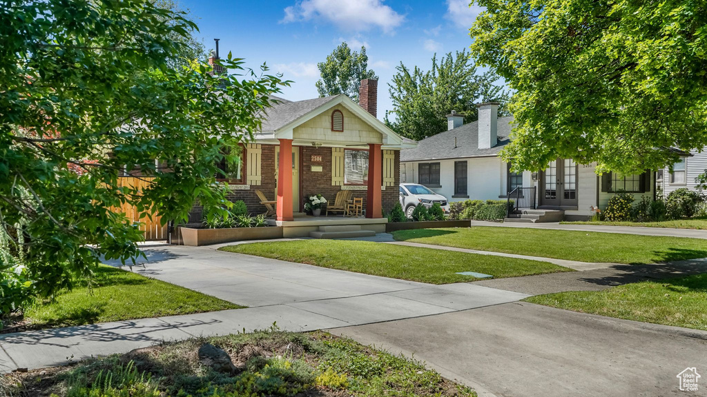View of front of property with brick siding, a front lawn, a chimney, a porch, and french doors