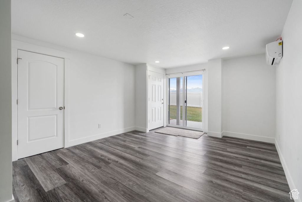 Empty room featuring a wall mounted AC, wood finished floors, baseboards, and recessed lighting