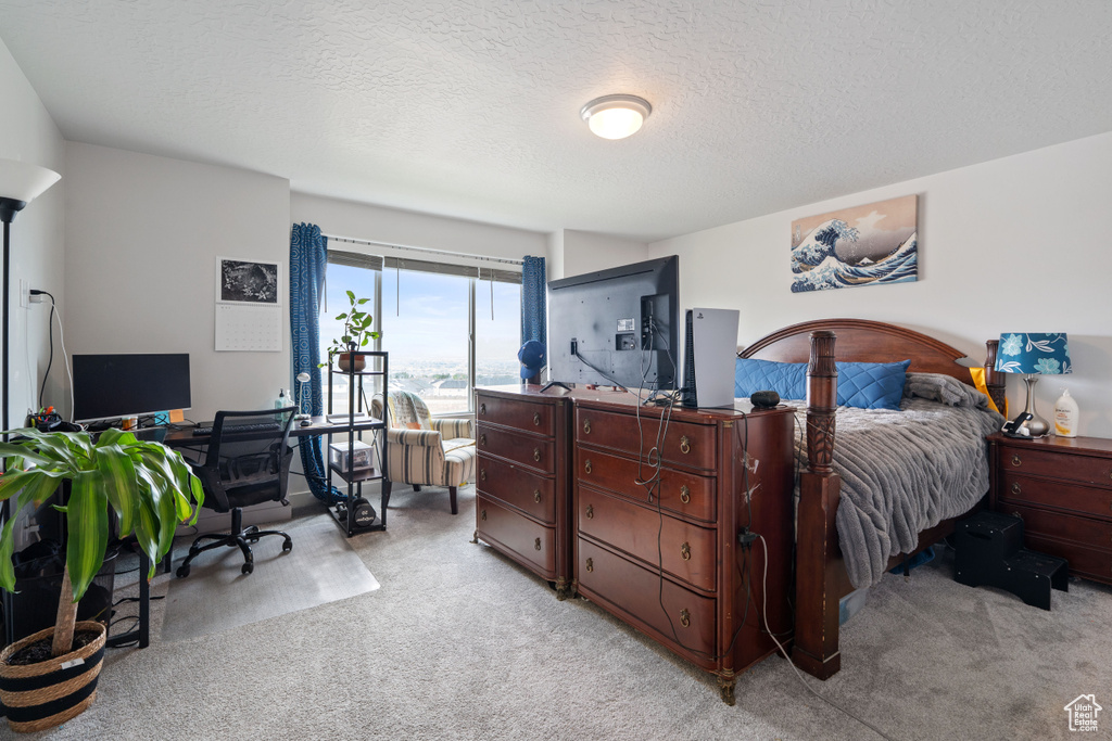 Bedroom featuring light carpet, an office area, and a textured ceiling