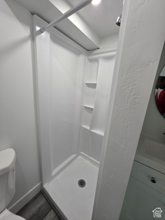 Full bath featuring a shower stall, wood finished floors, toilet, and baseboards