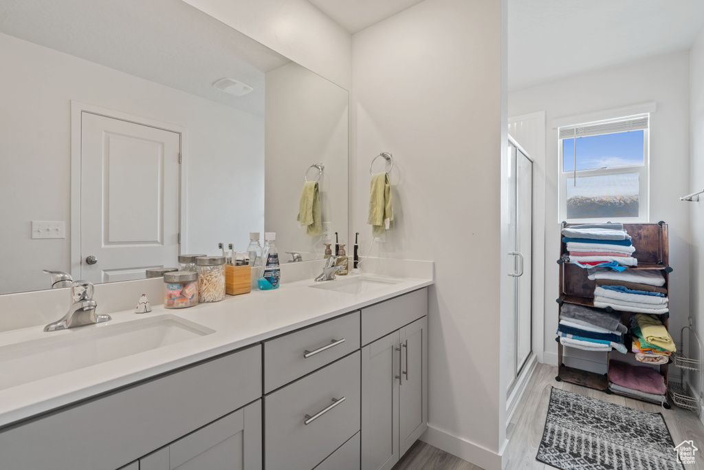 Bathroom with double vanity, a stall shower, wood finished floors, and baseboards