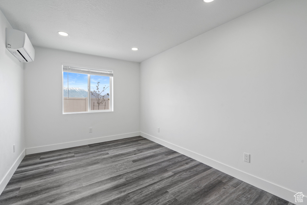 Empty room with a wall unit AC, recessed lighting, dark wood finished floors, and baseboards