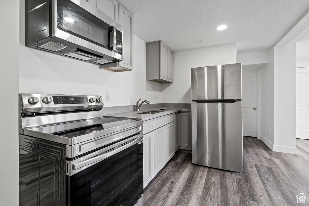 Kitchen featuring appliances with stainless steel finishes, a sink, wood finished floors, gray cabinetry, and recessed lighting