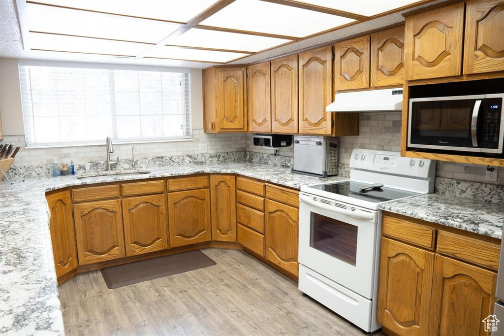 Kitchen featuring white electric stove, under cabinet range hood, stainless steel microwave, a sink, and tasteful backsplash