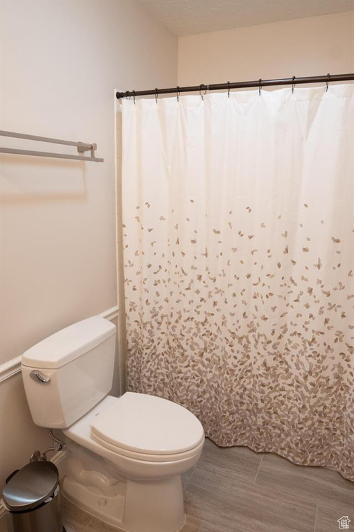 Full bathroom with toilet, wood finished floors, and a shower with curtain