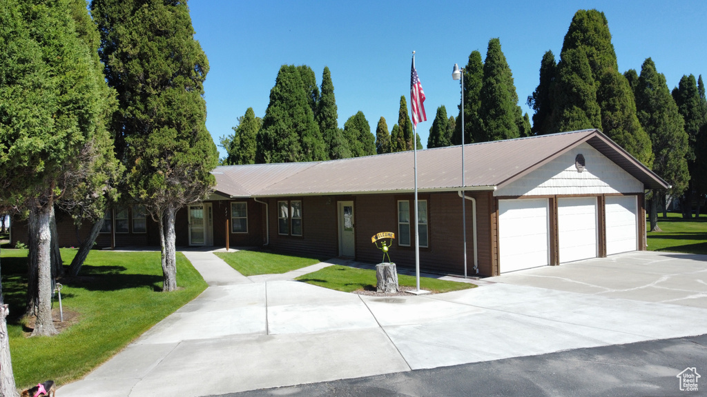 Single story home featuring a garage, concrete driveway, a front yard, and a metal roof