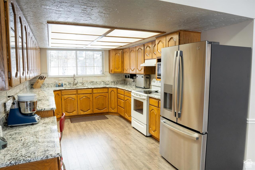 Kitchen featuring stainless steel refrigerator with ice dispenser, white range with electric stovetop, brown cabinetry, light wood-style floors, and under cabinet range hood