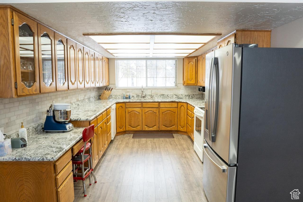 Kitchen with freestanding refrigerator, a sink, backsplash, light wood-style floors, and brown cabinetry