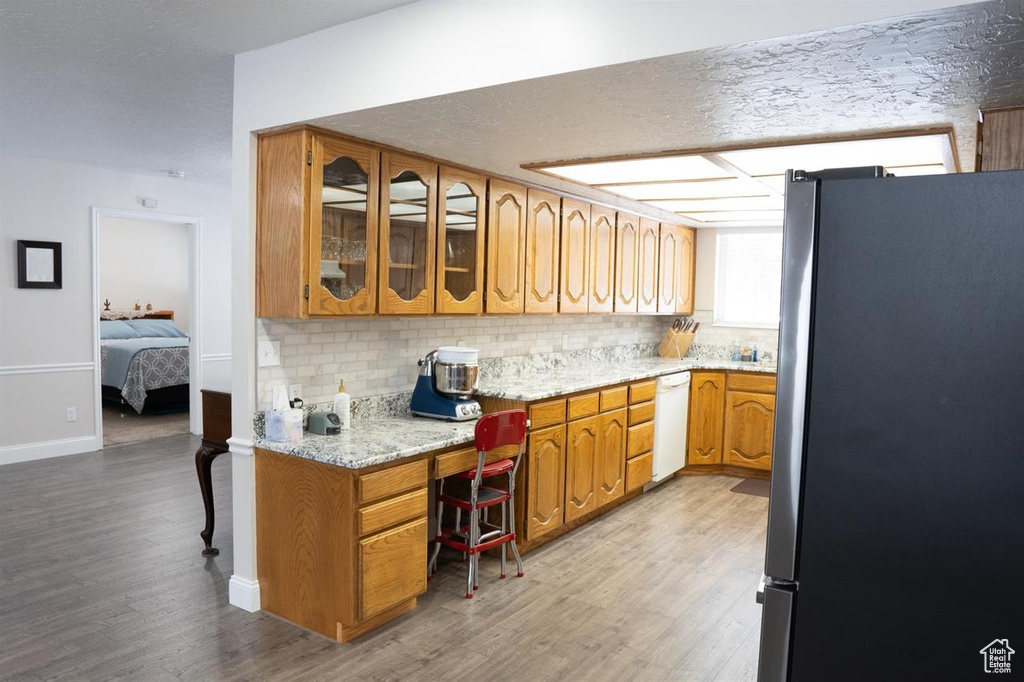 Kitchen with freestanding refrigerator, white dishwasher, wood finished floors, and decorative backsplash